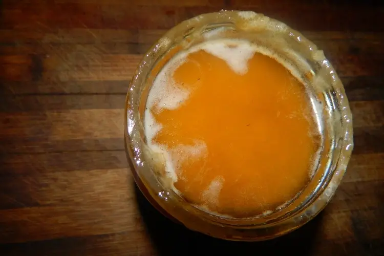 Open jar of honey with a thin layer of foam on the surface which is a sign of fermentation
