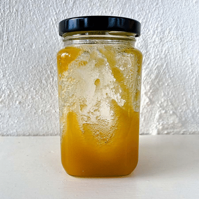 Glass jar of raw honey that has crystallized against a white wall background