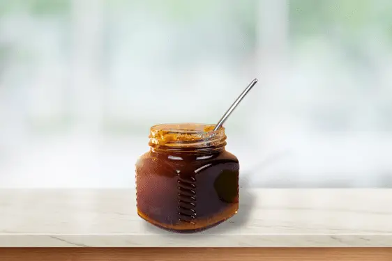 A jar of buckwheat honey with a spoon inside sitting on a kitchen counter